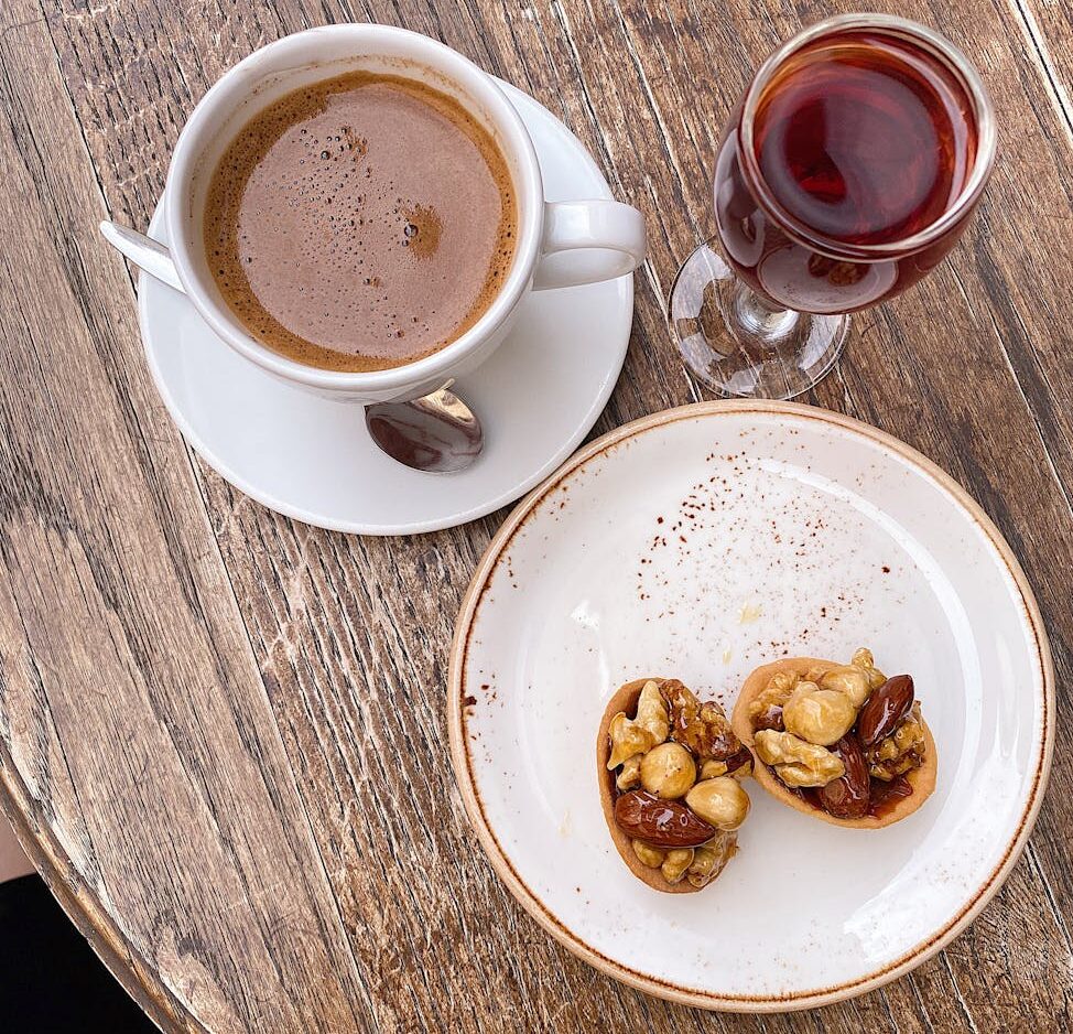 a cup of coffee nut dessert and liqueur on a wooden table